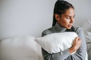 A woman holding a pillow with distress in her eyes trying to calm her anxiety.
